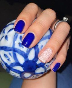 Uñas cortas de gel en azul con una uña en diseño de blancos